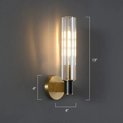 A minimalist brass finish tubular wall light sconce with a gold-toned base and clear glass cylinder for bedroom use