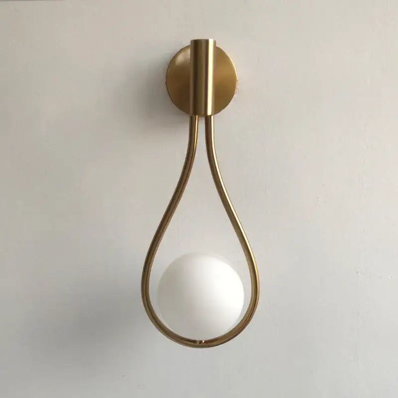 A minimalist brass glass ball wall sconce with a teardrop frame and frosted white spherical bulb for living room decor