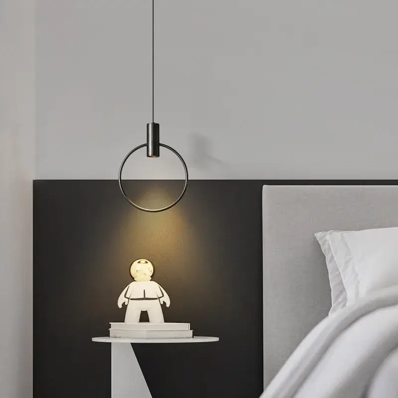 Minimalist brass ring chandelier with warm gold pendant light illuminating a white astronaut figurine on bedside table