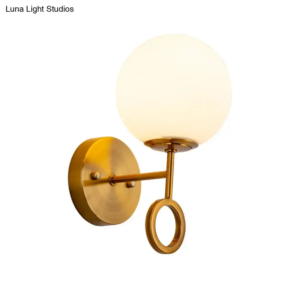 Minimalist brass wall sconce with gold tone finish and cream glass shade featuring frosted globe and circular accent ring