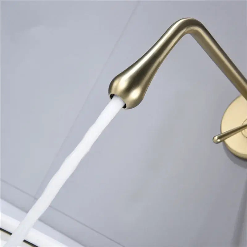 Minimalist brushed gold basin faucet with sleek teardrop design and flowing water stream for bathroom wall mounted use