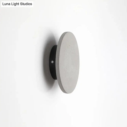 Minimalist cement grey flat round wall sconce light with a concrete disc and sleek black mounting base for bedroom use