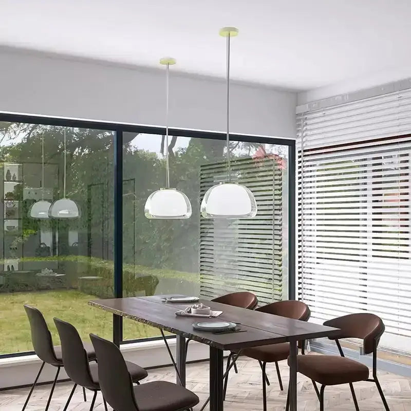 Two modern jelly pendant lamps with clear glass dome shades and slender metallic chains hang above a dining table