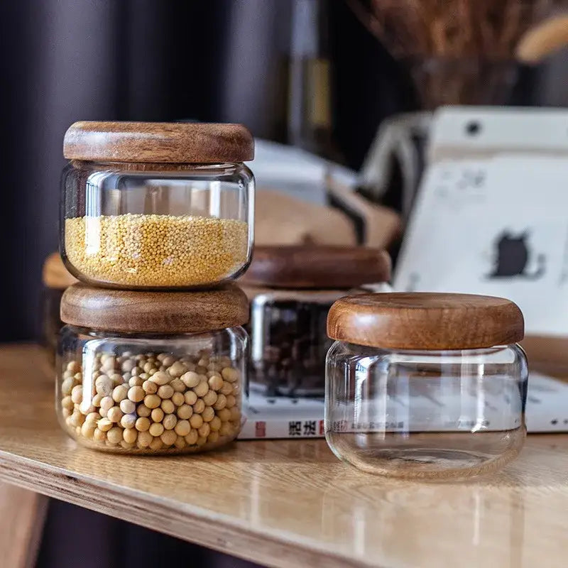 Minimalist clear glass storage jars with smooth rounded acacia wood lids on countertop for kitchen organization