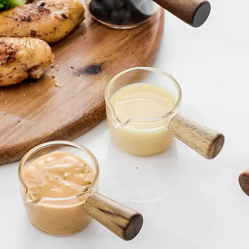 Minimalist clear glass sauce dish with wooden handle featuring two glass sauce cups holding different colored dressings