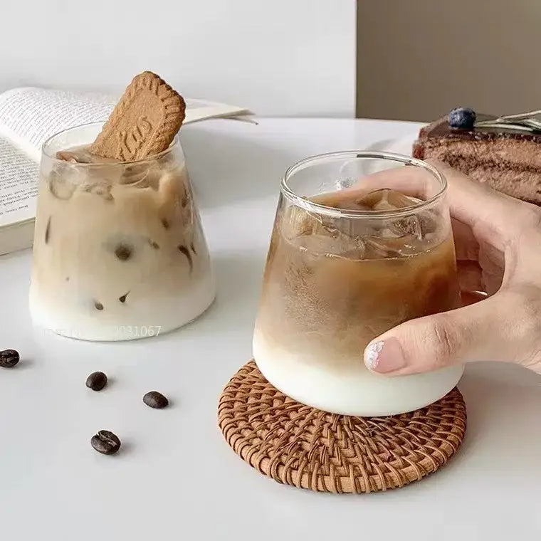 Minimalist clear glass water cup with rounded base filled with iced coffee showcasing layered brown liquid over milk
