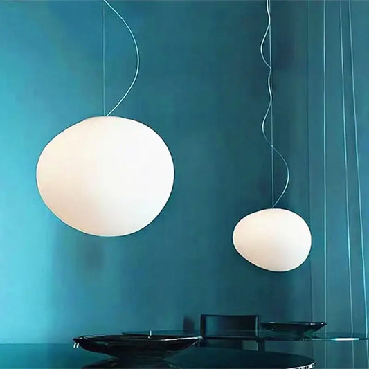 Two white acrylic pendant lights with spherical design and white finish hang against teal wall for dining room use