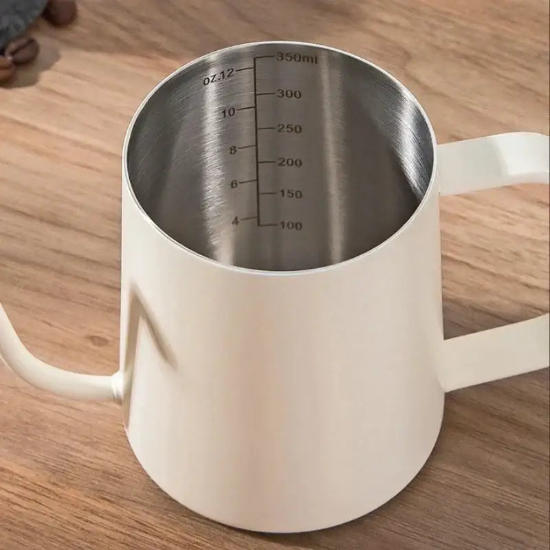 White ceramic milk frothing pitcher with stainless steel interior and measurement markings for glass coffee maker use
