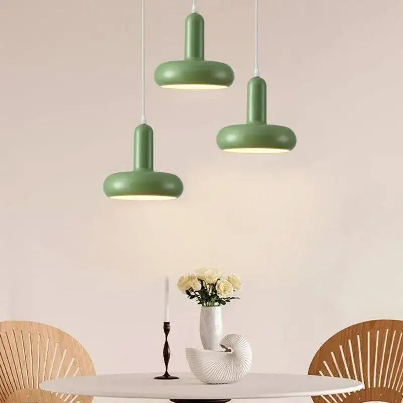 Three modern cream white ceramic pendant lights with decorbites disc shaped design hang above a dining table