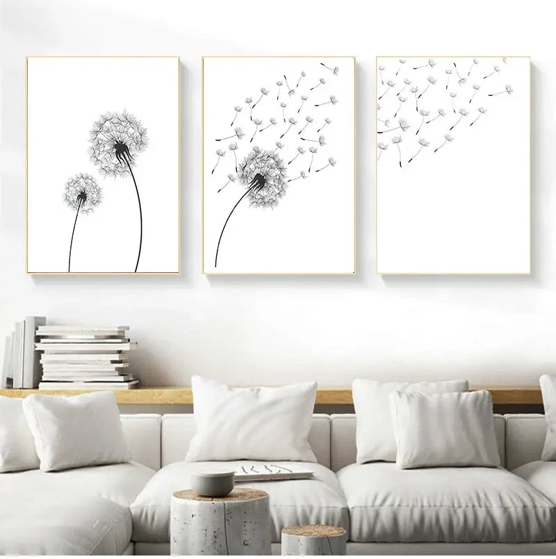 Three minimalist dandelion black-and-white canvas wall art prints with thin gold frames above a white sofa by DecorBites