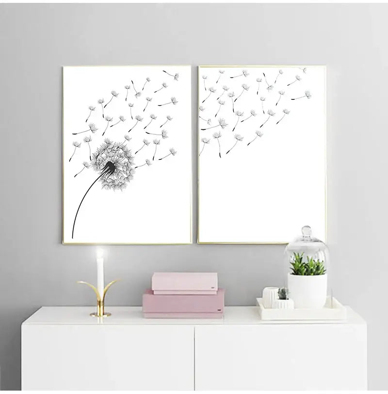 Two framed minimalist dandelion black and white canvas wall art pieces in gold frames hanging above a white cabinet