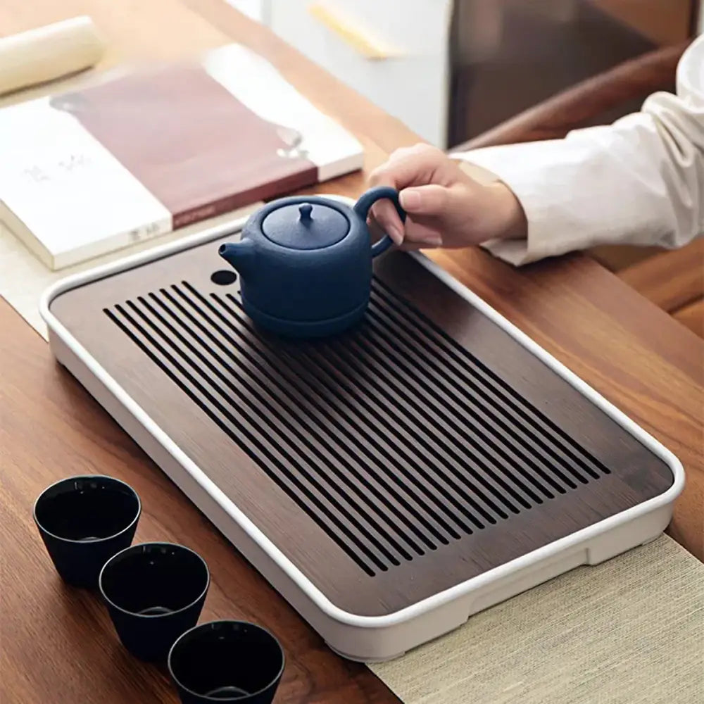 Dark blue ceramic teapot with matching lid and handle resting on minimalist dark brown and black bamboo tea tray