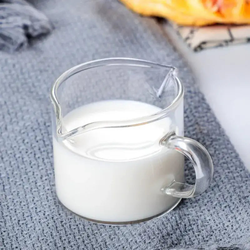 Clear glass double mouth glass pitcher filled with white liquid on textured gray surface for kitchen use