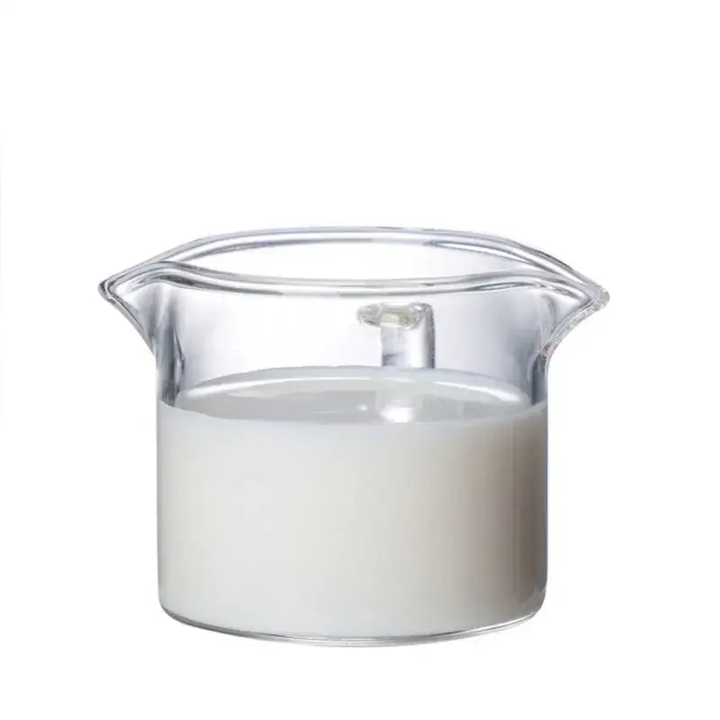 Clear glass double mouth glass milk cup filled with white liquid from minimalist kitchen pitcher set