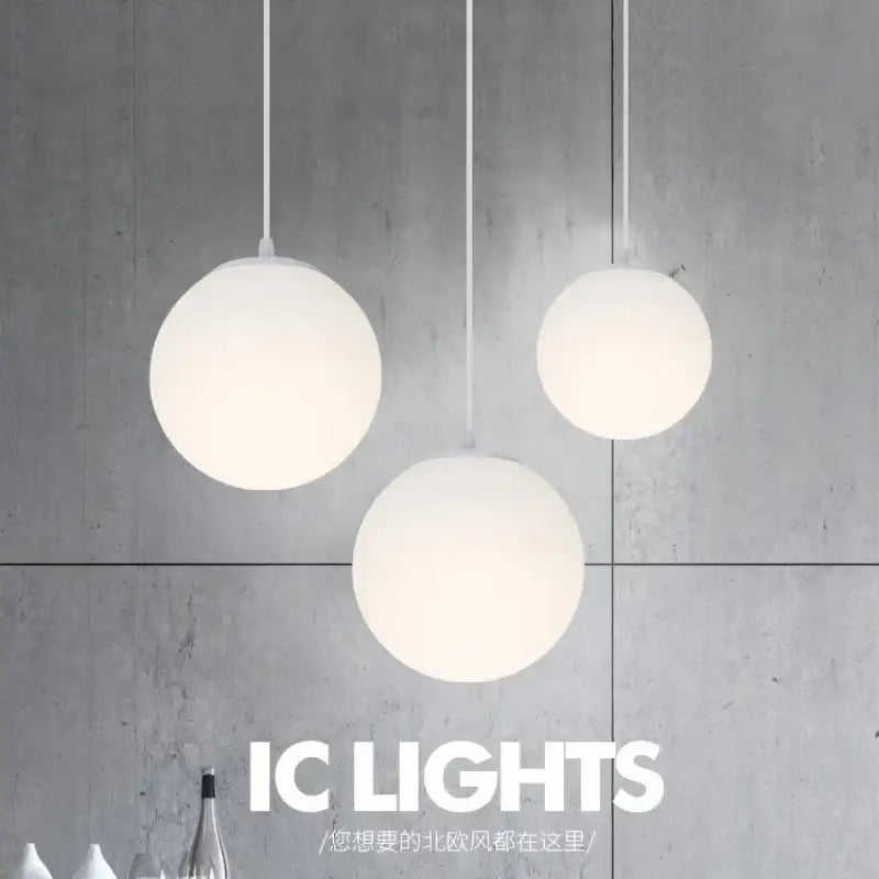 Three minimalist frosted white acrylic globe pendant lights with brushed nickel cords hang against a concrete wall