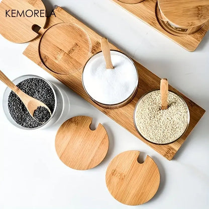 Minimalist glass spice jar set with bamboo lids and wooden spoons arranged on a matching bamboo tray for kitchen organization