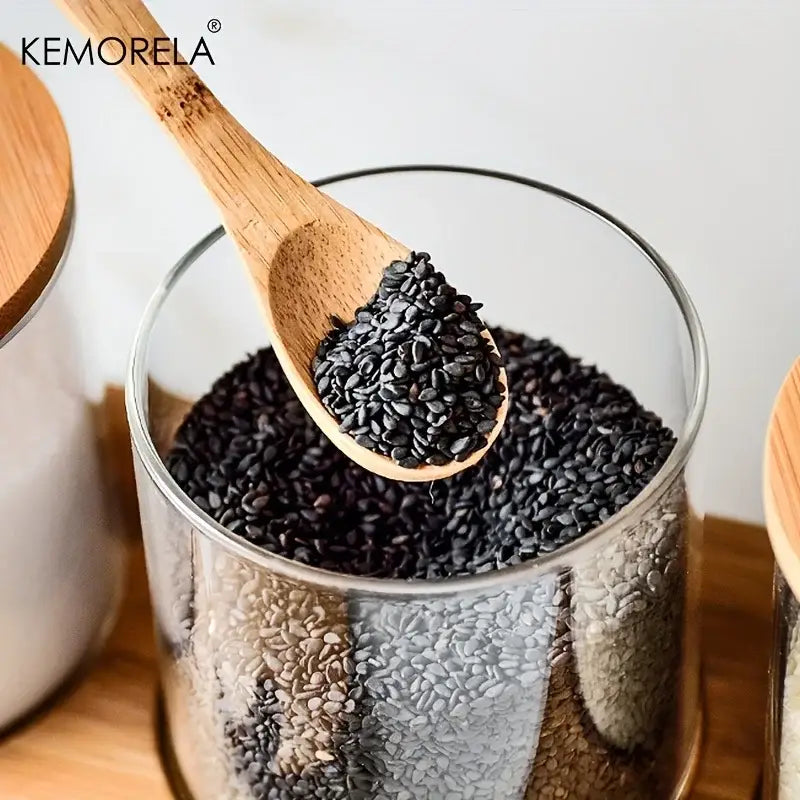 Minimalist glass spice jar set with bamboo lids showing a clear glass spice jar filled with black sesame seeds and wooden spoon