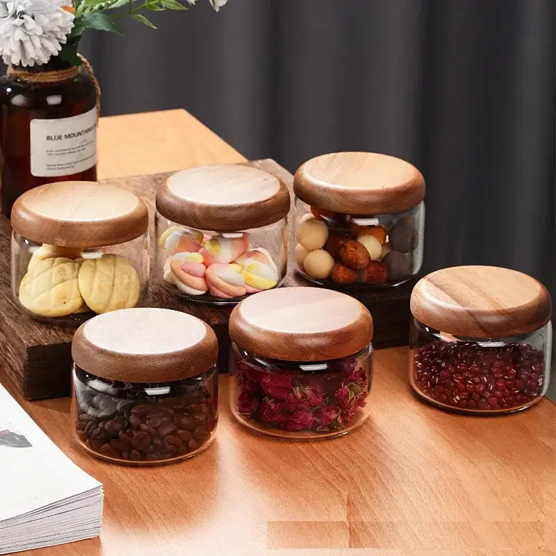 Set of six clear glass spice jars with acacia wood lids containing dried goods for kitchen storage