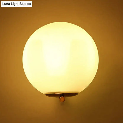 Minimalist bedroom wall sconce with warm white light featuring frosted white glass ball and brass-finished mounting hardware