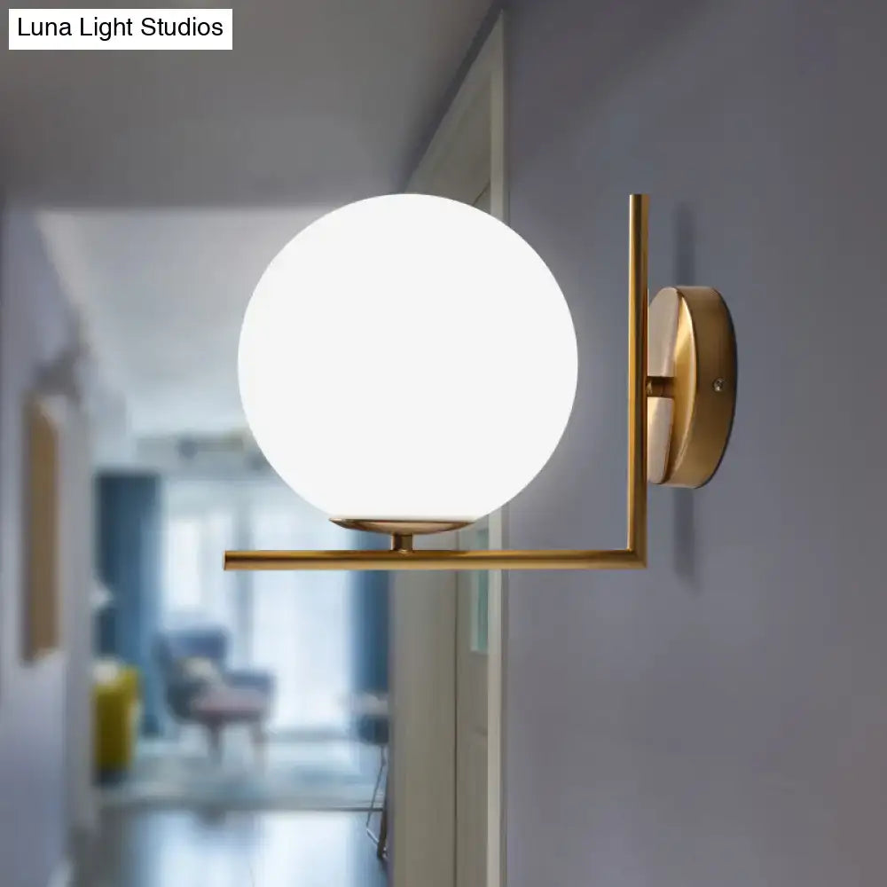 Minimalist gold-toned wall sconce with frosted white glass ball providing warm white light for bedroom use