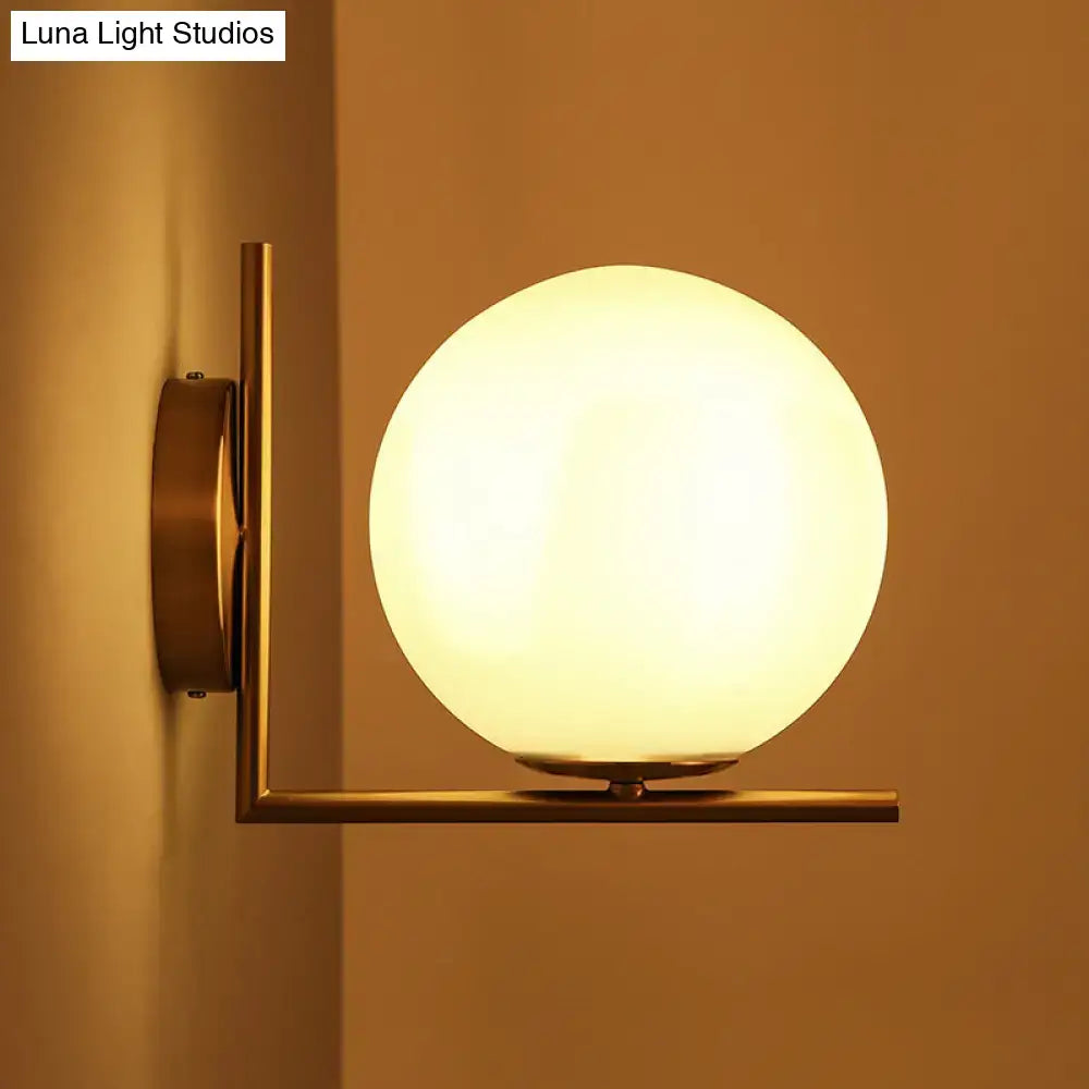 Minimalist warm-toned brass wall sconce with a frosted white glass ball providing warm white light for bedrooms