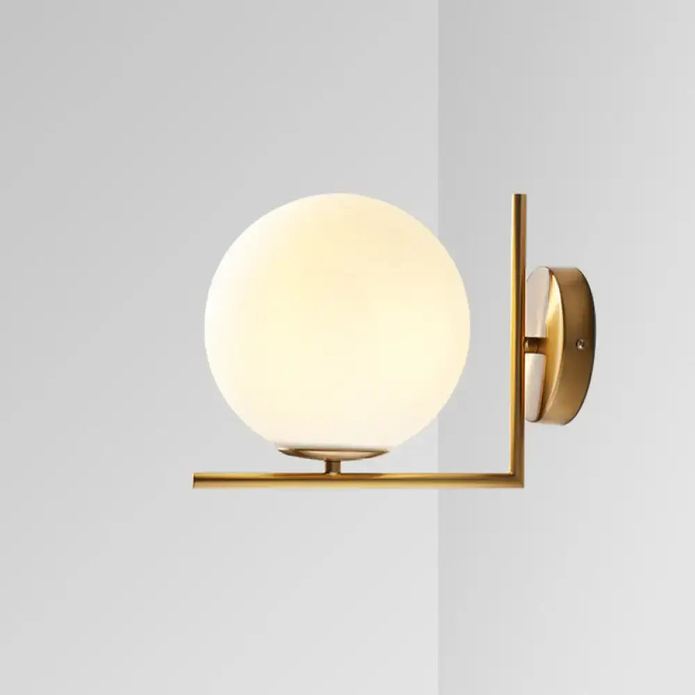 Minimalist gold wall sconce with frosted white glass ball emitting warm white light for bedroom lighting