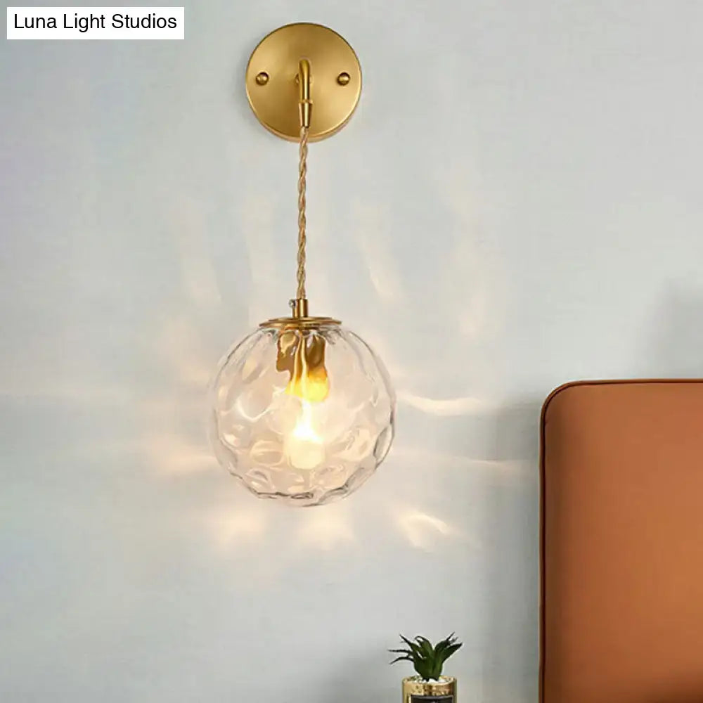 Minimalist gold ball sconce with hammered glass shade featuring a textured clear globe and twisted brass chain