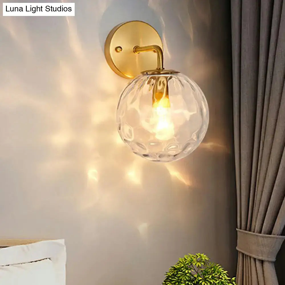 Minimalist gold ball sconce with hammered glass shade featuring a textured clear glass globe for bedroom lighting