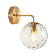 Minimalist gold ball sconce with hammered glass shade and brass hardware featuring a textured clear globe