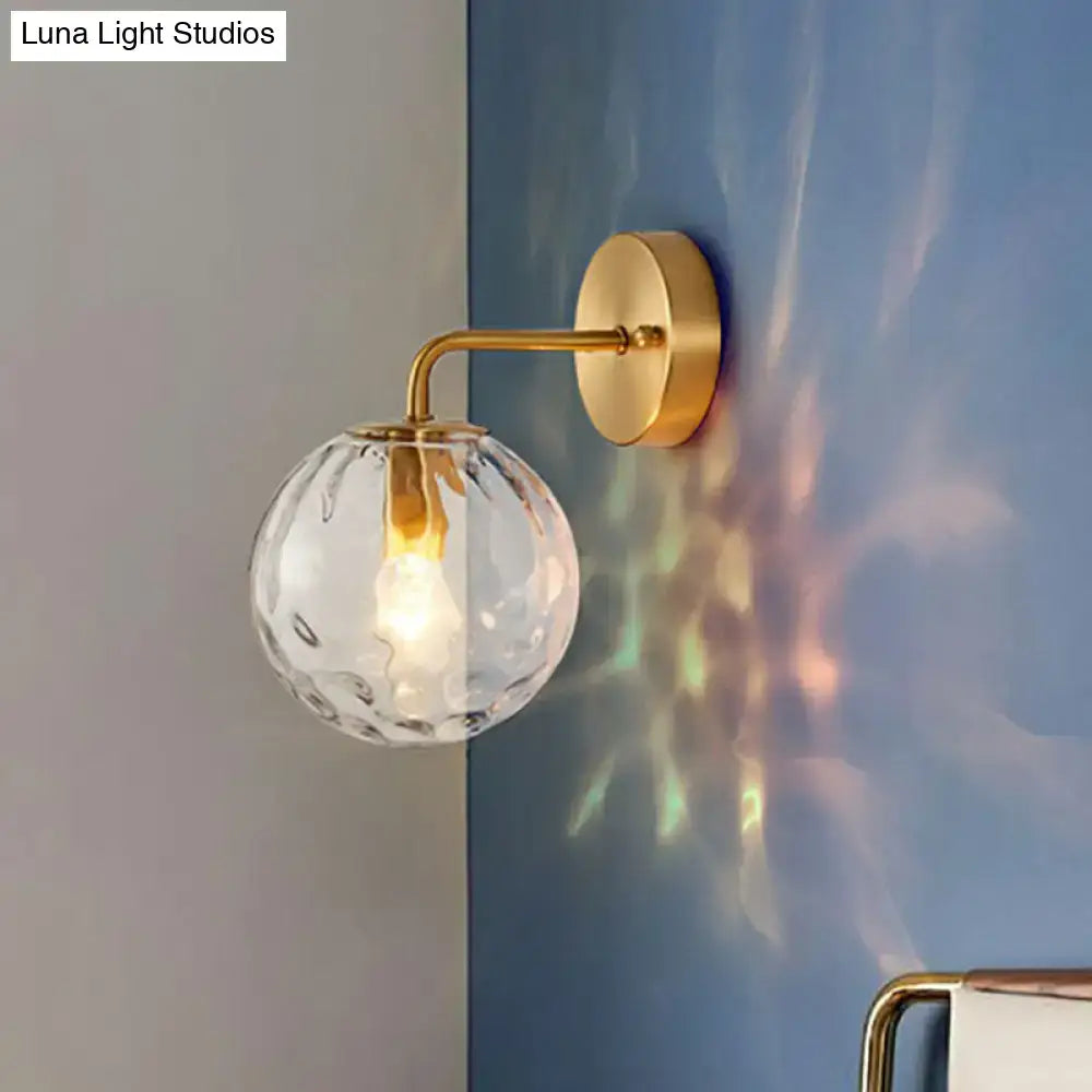 Minimalist gold ball sconce with hammered glass shade featuring a gold-toned textured glass globe for bedroom lighting