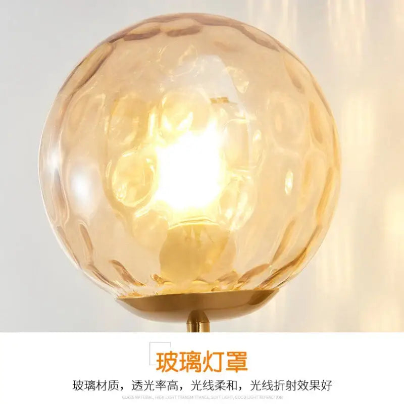Minimalist wall lamp featuring a warm amber decorbites glass ball led with textured hammered surface and gold metal base
