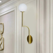 Minimalist gold-toned wall sconce with frosted opal glass globe and long curved arm for bedroom lighting