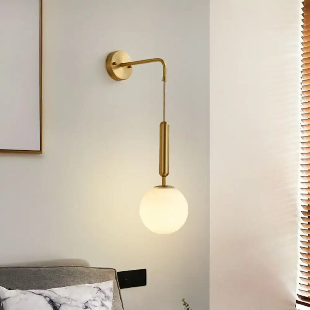 Minimalist gold finish wall light with a sleek curved arm and cream glass frosted globe shade for bedroom use