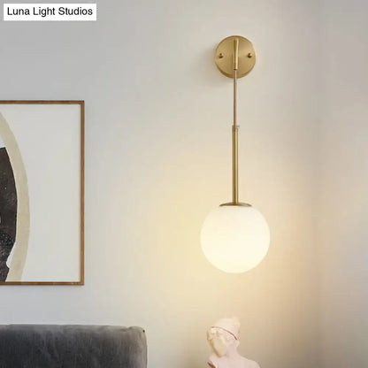 Minimalist wall light with gold finish and cream glass globe shade featuring a slender rod design for bedroom use
