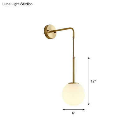A sleek brass finished wall light with a curved arm and cream glass globe shade for bedroom use