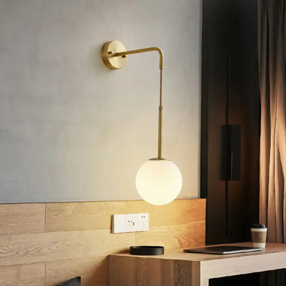 Minimalist gold finish wall light with a curved arm and cream glass spherical shade for bedroom lighting