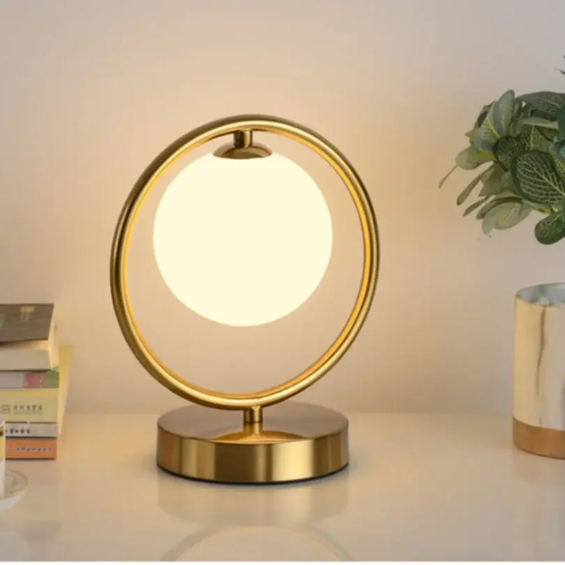 Minimalist gold glass ball led table lamp with a glowing white spherical bulb in a metallic ring for bedroom decorbites decor