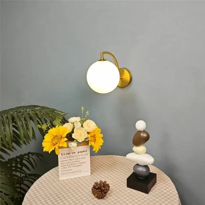 Minimalist gold wall sconce with a matte white glass ball globe designed as a bedroom wall lamp fixture