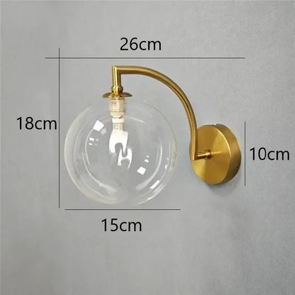 Minimalist gold-toned wall sconce with clear glass ball and exposed bulb ideal as a bedroom wall lamp