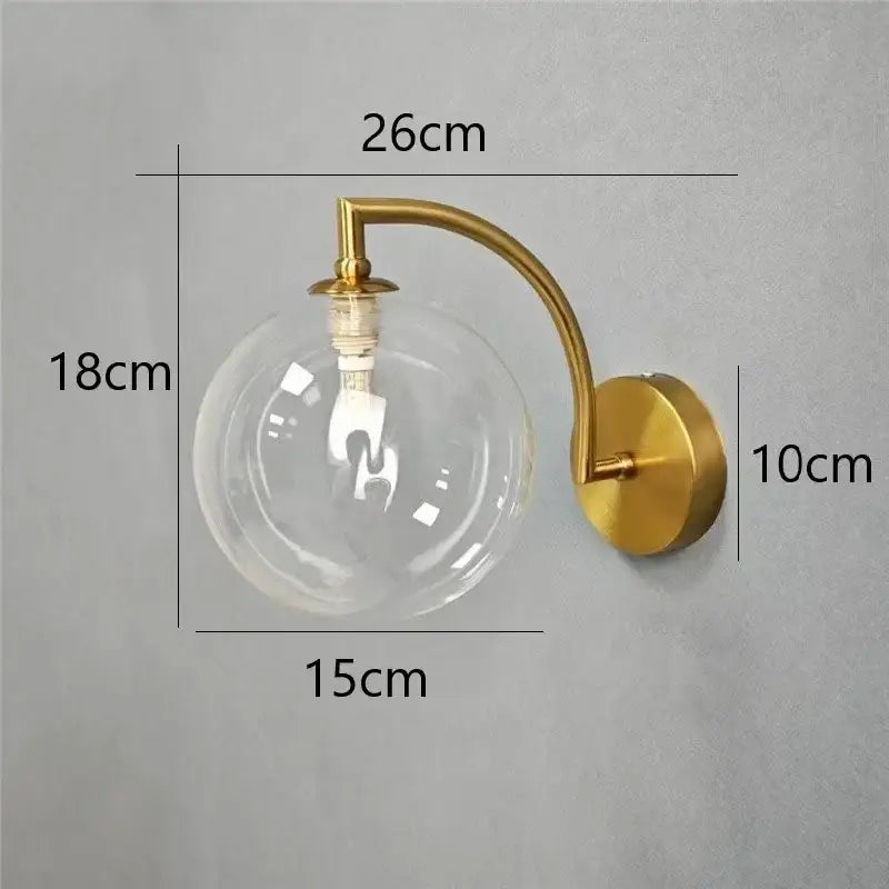 Minimalist gold-toned wall sconce with clear glass ball and exposed bulb ideal as a bedroom wall lamp