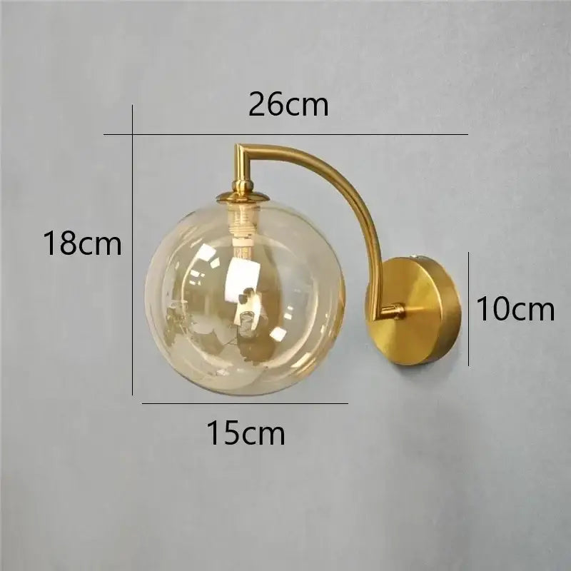 Minimalist gold wall sconce with clear glass ball and curved arm designed as a bedroom wall lamp