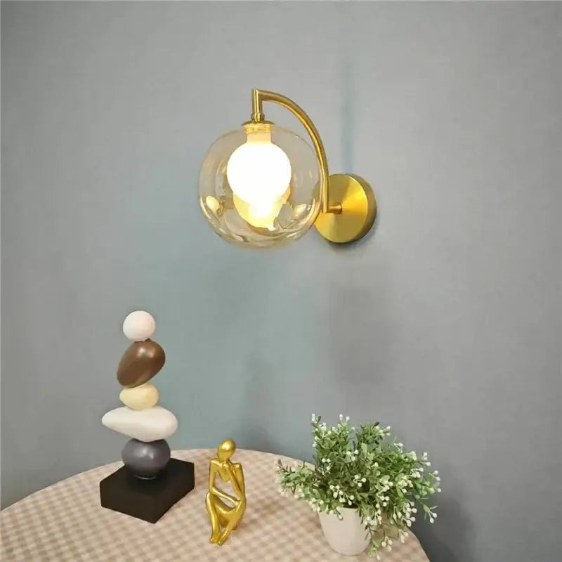 Minimalist gold wall sconce with a glass ball globe and illuminated bulb ideal as a bedroom wall lamp