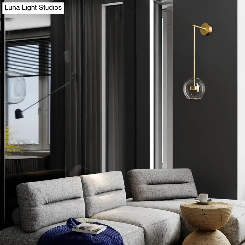 Minimalist gold-toned wall hanging light with a clear glass globe and slender metallic arm for bedroom use