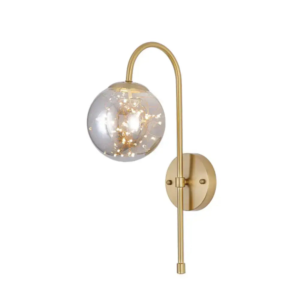 Minimalist gold wall light with gooseneck arm and smoke gray amber spherical globe containing fairy lights for bedroom