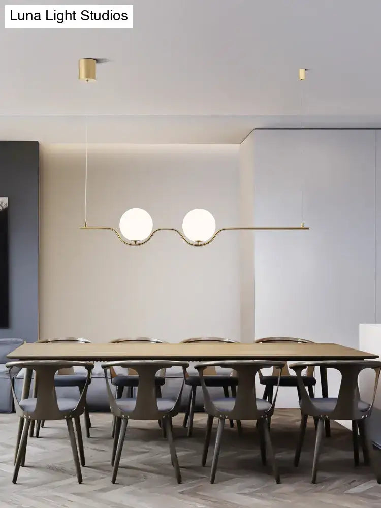 Minimalist gold metal island pendant ceiling light with two white glass bulbs above a dining table