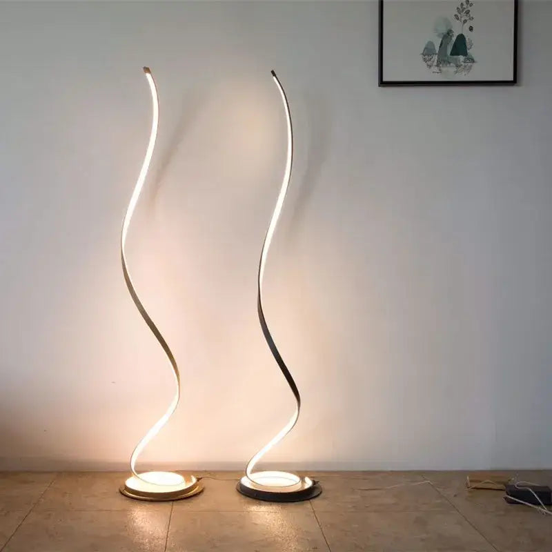 Two sleek minimalist standing lamps with curved glowing white led strips and circular gold toned bases for living room use