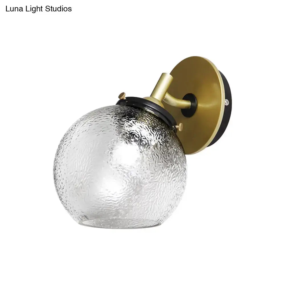 Minimalist gold water glass wall sconce with textured clear glass globe for living room mounted on brass and black fixture