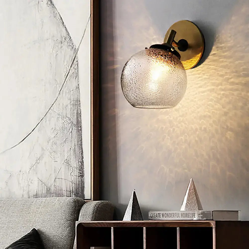 Minimalist gold-toned wall sconce with textured frosted glass globe for living room lighting and decor