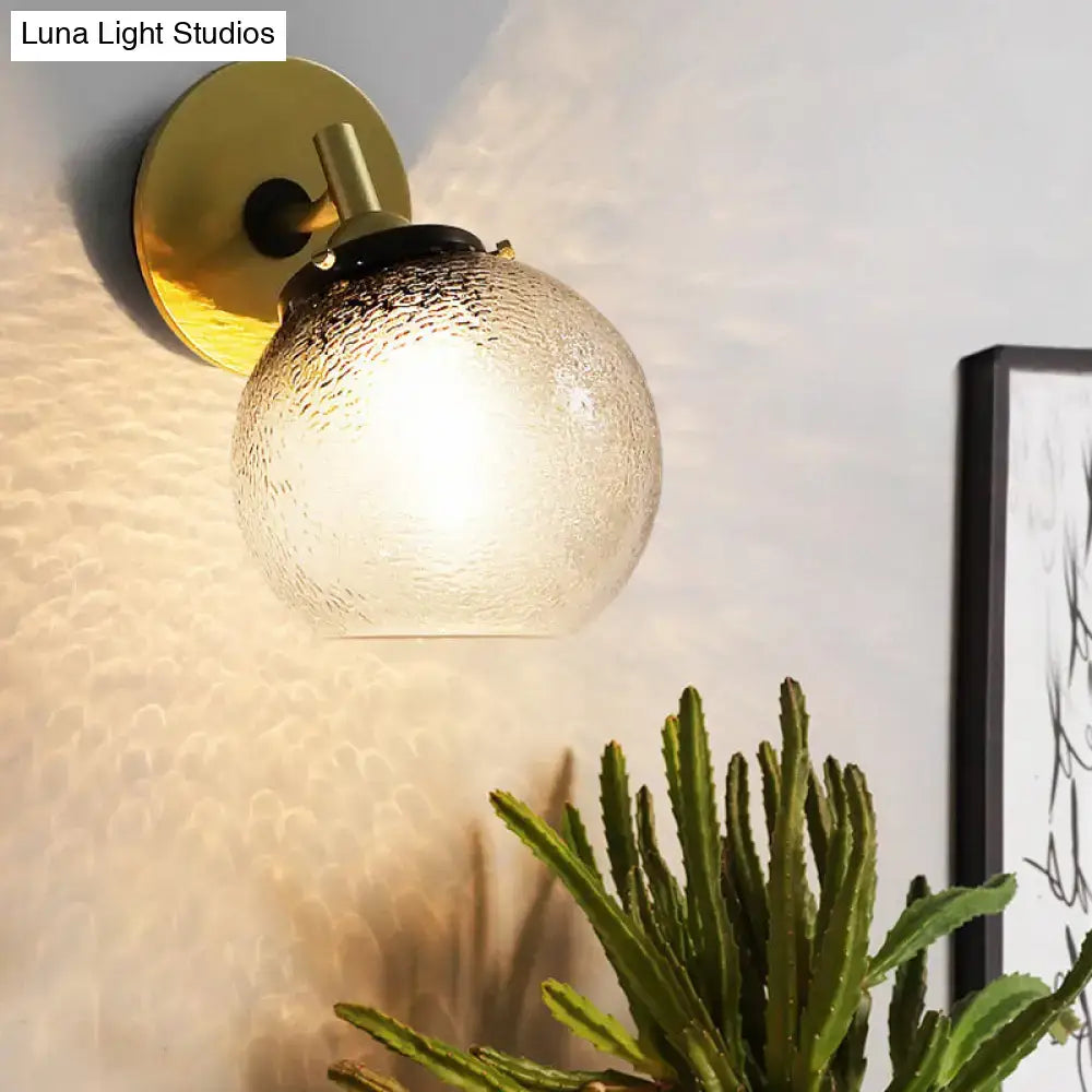 Minimalist gold-toned wall sconce with textured frosted glass globe for stylish living room lighting