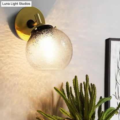 Minimalist gold-toned wall sconce with textured frosted glass globe for stylish living room lighting